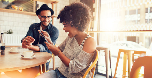 Happy woman using a tablet while hanging out with a friend at a cafe