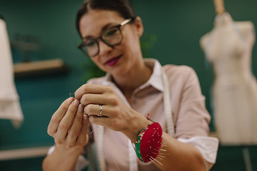 Female dressmaker putting thread into needle