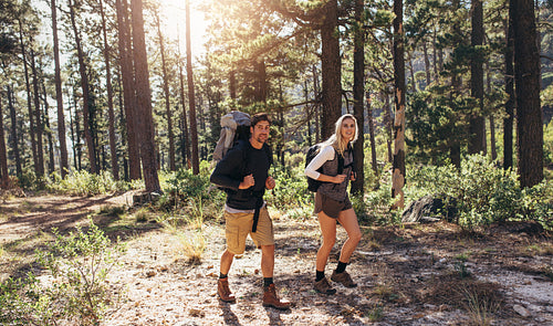Hiking couple walking in forest wearing backpacks