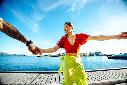 Holding hands, woman turns with a friend by the waterfront in summer
