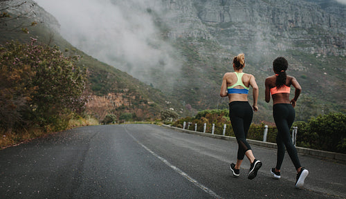 Two women athletes running on road