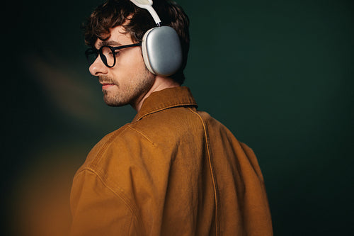 The man wears headphones and glasses in a casual green studio profile
