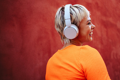 Woman smiles with music on headphones against a red background
