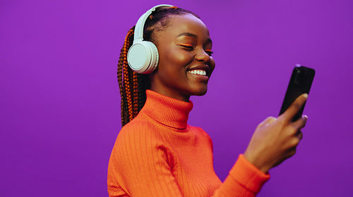 Happy gen z girl listening to music with headphones and browsing on smartphone
