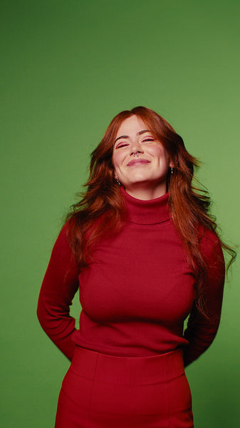 Happy young woman with long red hair waves and smiles on green screen