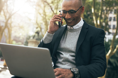 Businessman using laptop and mobile phone sitting outdoors