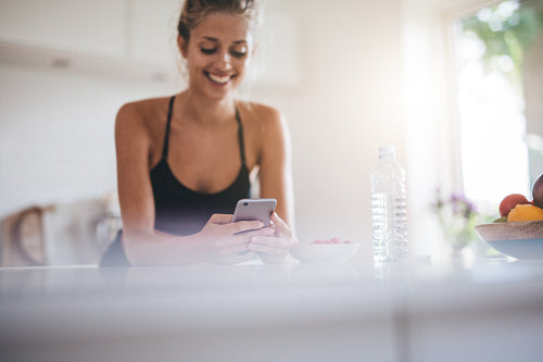 Smiling woman having breakfast and using cell phone in kitchen