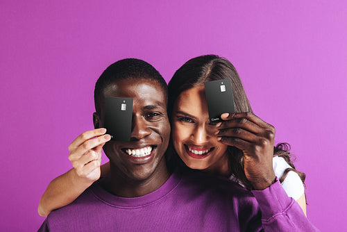 Happy couple holding black credit cards in a studio, recommending electronic banking