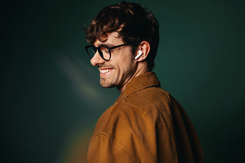 Casual business man with glasses and earbuds smiles in studio profile
