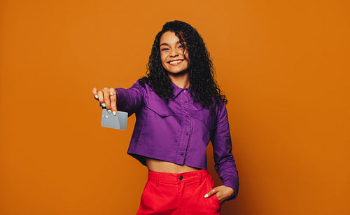 Cheerful woman smiling doing a swiping gesture with her credit card on a vibrant orange background
