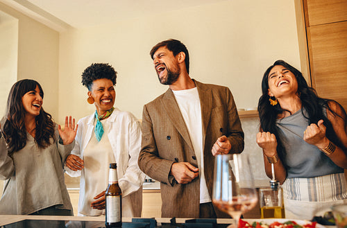 Group of friends laughing and singing together in a cozy home kitchen