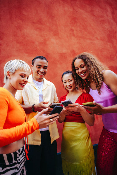 Friends use smartphones together outdoors against a bright wall