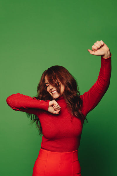 Stylish woman celebrating Christmas with carefree dance moves on vibrant green background