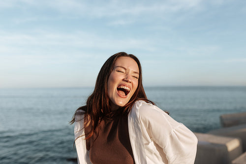 Outdoorsy brunette laughing with her eyes closed by the seaside