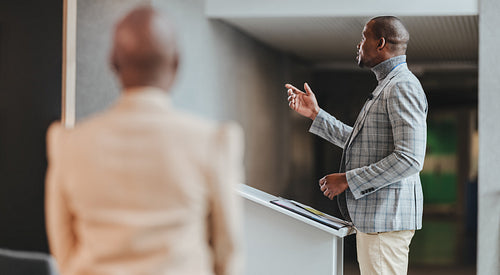 Confident businessman giving presentation at conference, engaging audience with speech, professional corporate event