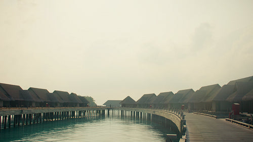 Peaceful overwater villas in a luxury tropical resort with calm turquoise waters under a hazy sky