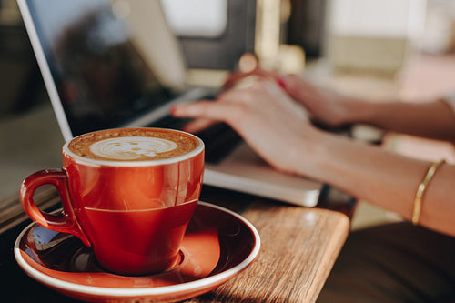 Cup of coffee on table with woman using laptop