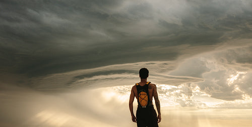 Fit man taking rest after workout against dramatic sky