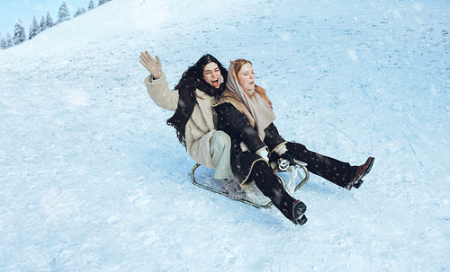 Laughing women sledding with friends on a snowy hill