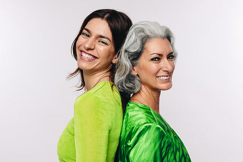 Mother and daughter standing back to back smiling