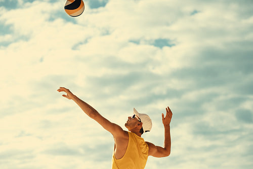 Beach volleyball player raising arms to block a mid-air ball in summer sports tournament