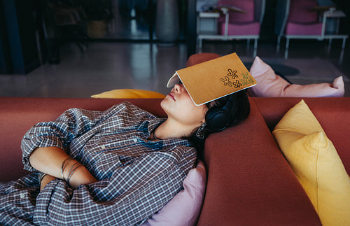 Tired high school student resting on a couch with a book on their face after exams, embodying fatigue and need for relaxation