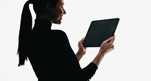 Silhouette of a woman holding a digital tablet wearing a black outfit