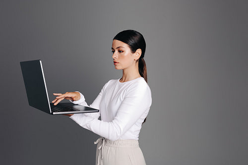 Professional woman using a laptop while standing against a studio background