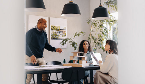 Team discussing architectural model during project management meeting in modern office