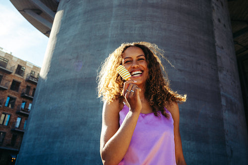 Sunny woman enjoys a popsicle outdoors by the city overpass in summer