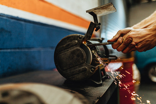 Mechanic grinding a car part on bench grinder