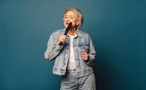 Dancing senior woman with grey hair enjoying music on a blue brush background