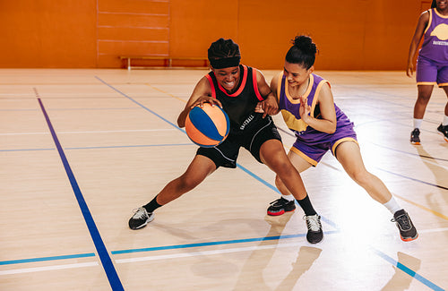 Two women competing for the basketball during an intense game in gym