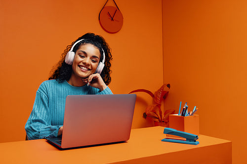 Young female student listening to music on headphones while working on laptop at desk