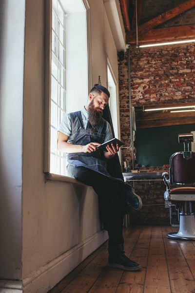 Young barber at his barbershop using digital tablet
