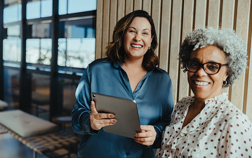 Women in business smile through a team meeting while using a tablet in the office