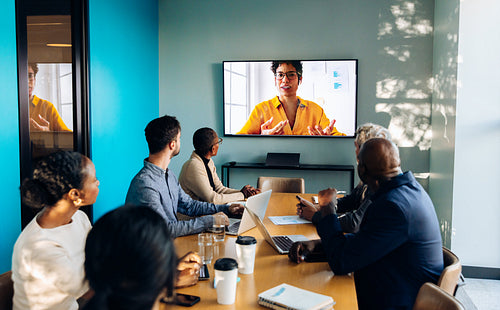 Team conducts meeting with video call participant displayed on large screen