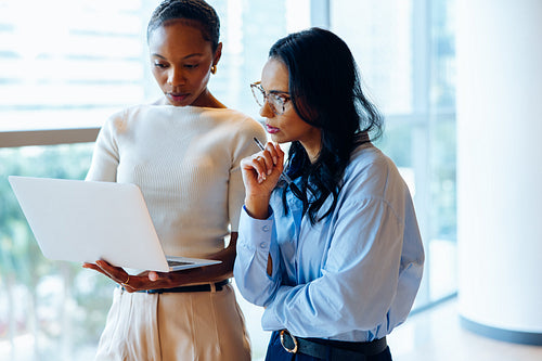 Two female professionals working together on a laptop in a bright office environment