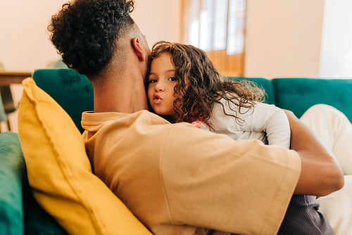 Cute little girl sitting in her father's arms at home