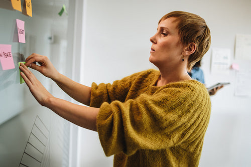 Female executive putting sticky note on glass