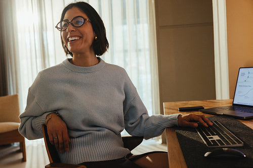 Woman smiles at her desk with a laptop in a bright office