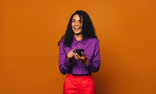 Vibrant woman smiling and browsing on a mobile phone against a cheerful orange background