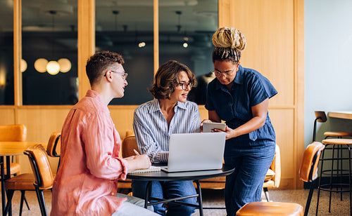 Team discussion with three adults using technology in a modern coworking space