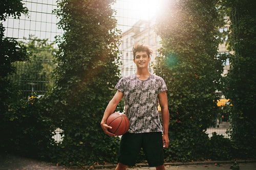 Young man holding a basketball on outdoor court
