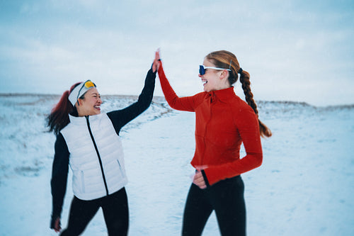 Women pause from running for a high five in winter snow