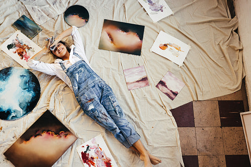 Overhead view of a painter lying in the middle of her paintings