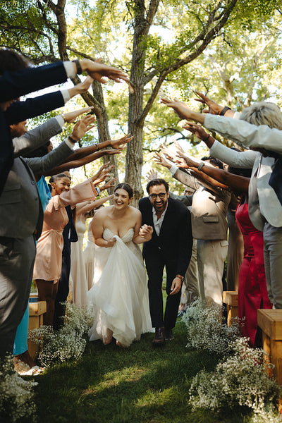 Joyful newlywed couple running through hand arch of friends in beautiful garden