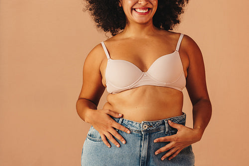 Happy young woman wearing a bra and jeans in a studio
