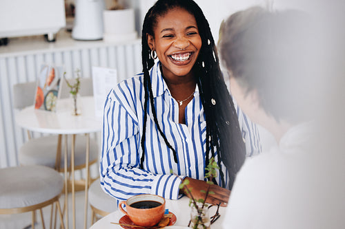 Cheerful young businesswoman having a coffee meeting with a female colleague in a cafe