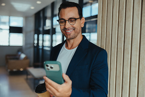 Smiling businessman using smartphone in a modern office hallway